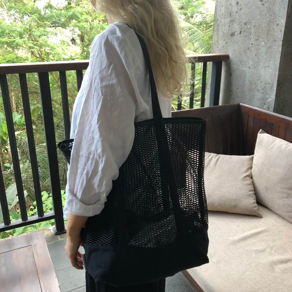 black canvas mesh tote on shoulder of girl with long blonde hair.  Standing on balcony with forest in background