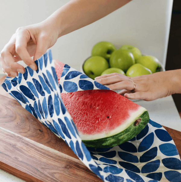 image of watermelon on a wooden chopping board being wrapped in a reusable blue and white patterned wax wrap