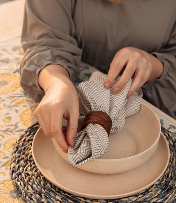 Picture of woman in grey dress holding beige and white handmade serviette folded over bowl with wooden serviette ring