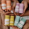 Hands holding various colored deodorant balm containers with visible brand labels.