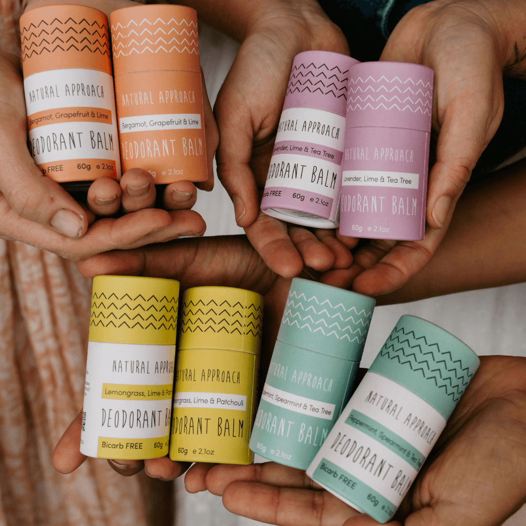 Hands holding various colored deodorant balm containers with visible brand labels.
