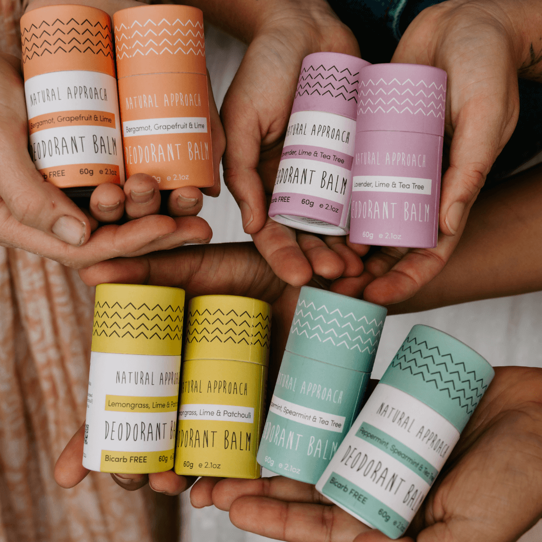 Hands holding various colored deodorant balm containers with visible brand labels.