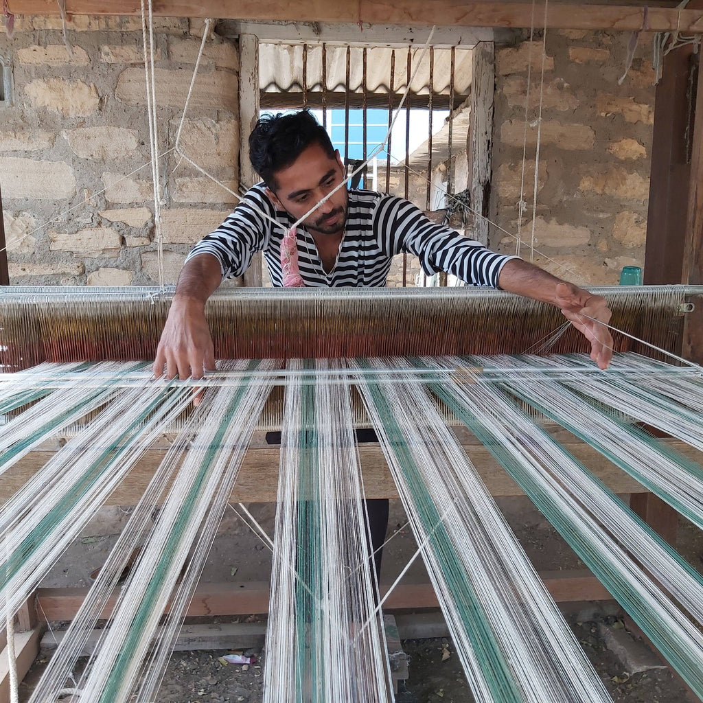 Indian artisan with dark hear pictured in striped top handweaving organic cotton napkins / serviettes