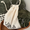 Calico Clothes Peg Bag with Drawstring and logo pictured with stainless steel pegs in laundry on towels