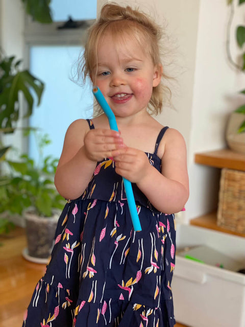 Little girl playing with colourful silicone straws in blue floral dress