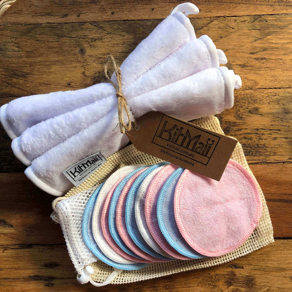 Set of reusable Bamboo Cotton makeup remover pads in various colours with a set of soft face and body care cloths, mini laundry bag and mini organic cotton produce bags, picture on a wooden surface.