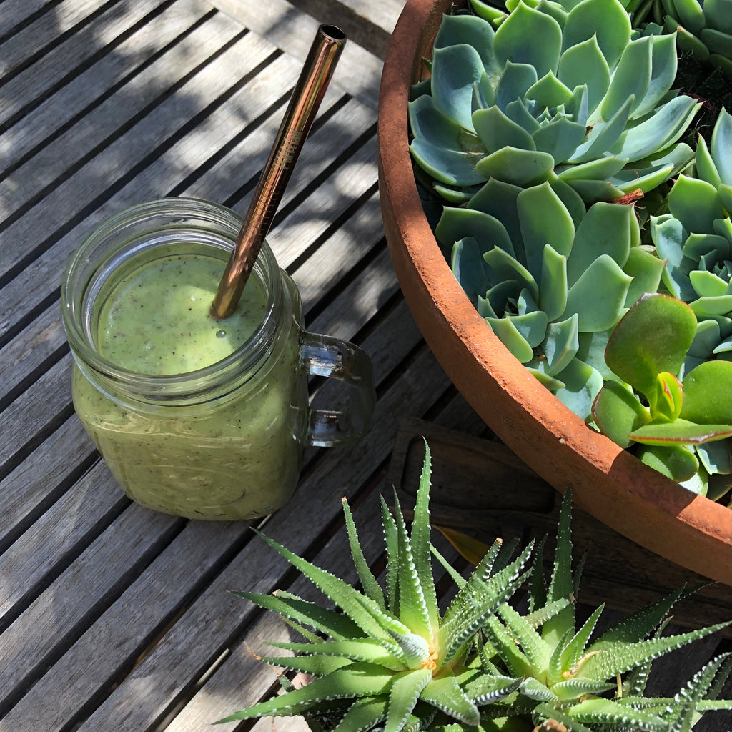 Green smoothie in a jar with a straw on a wooden surface next to a pot of succulents