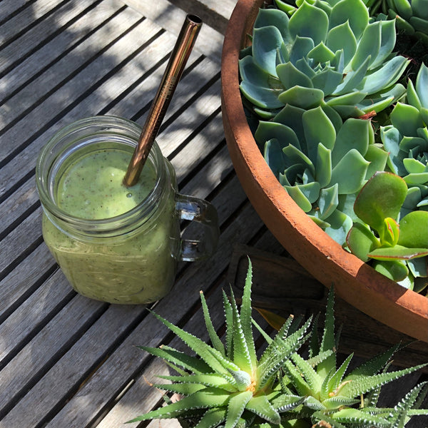 Green smoothie in a jar with a straw on a wooden surface next to a pot of succulents