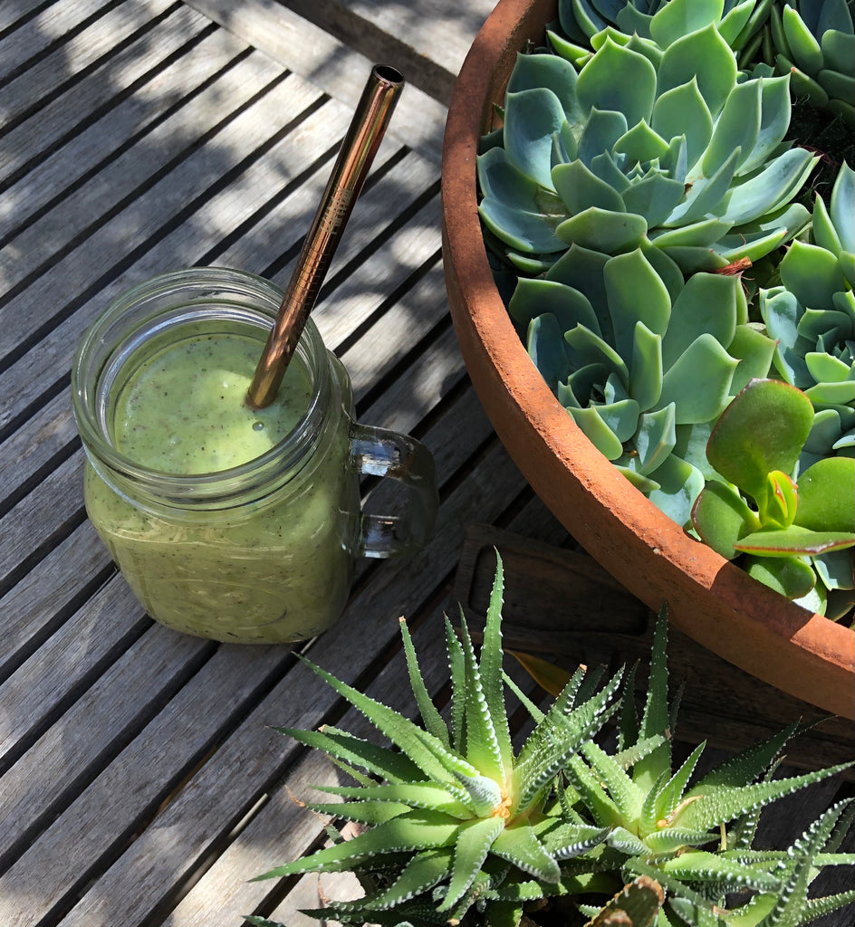 Green smoothie in a jar with a straw on a wooden surface next to a pot of succulents