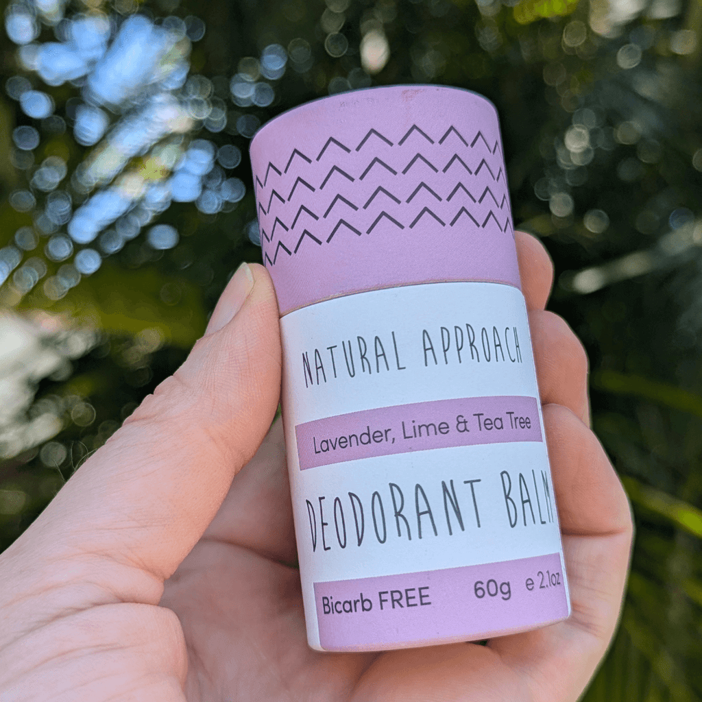 Hand holding a Natural Approach Lavender, Lime & Tea Tree deodorant balm with a blurred natural background of trees
